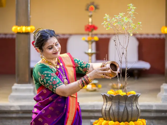 Offering water from a copper kalash to the tulsi vrindavan, dressed in traditional Paithani with marigold decor.