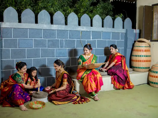 Traditional courtyard scene with women seated by the stone grinder (jaata) and stone battlements.