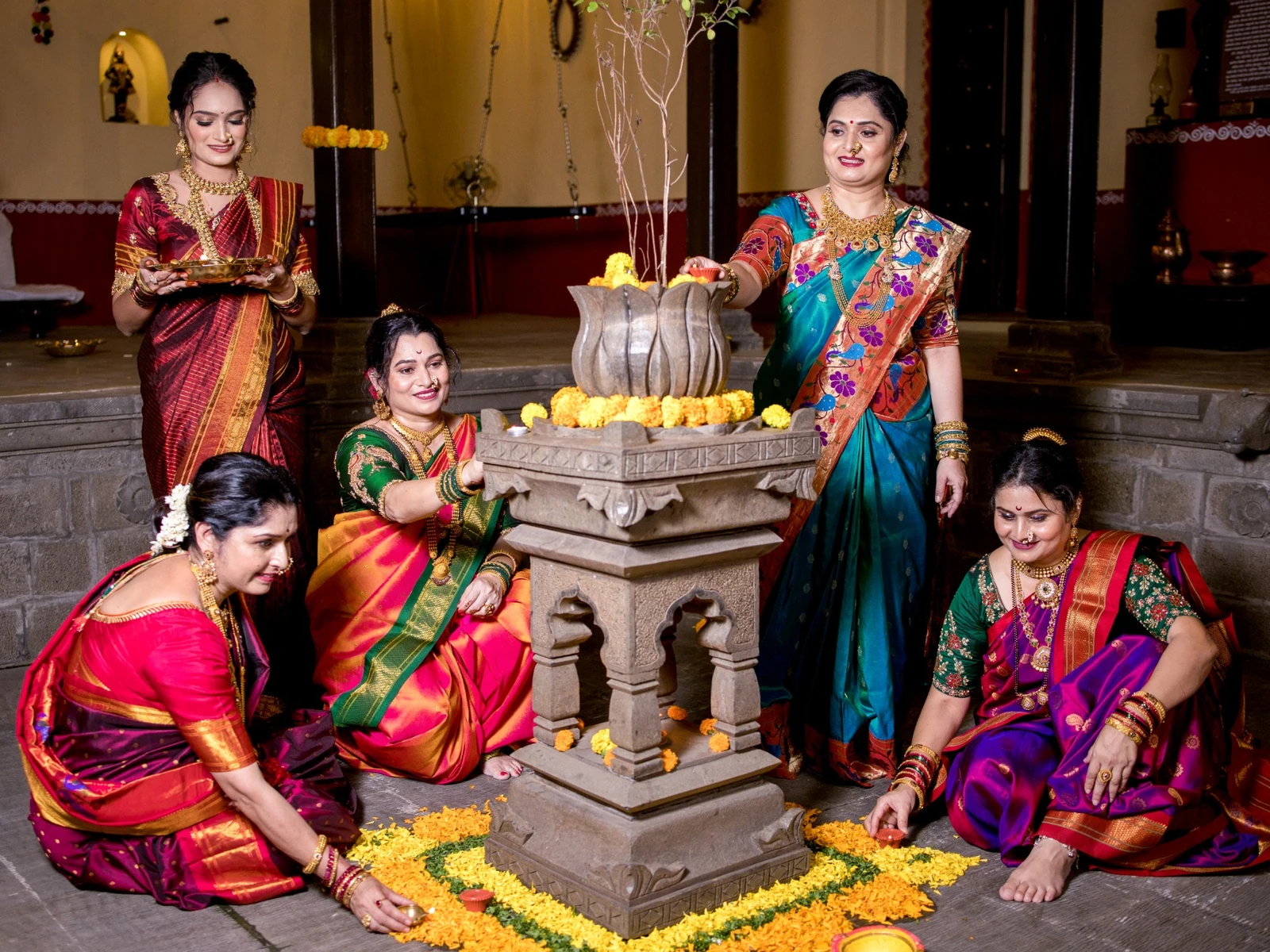 Lighting traditional clay oil lamps around the carved stone tulsi vrindavan during an evening ritual.