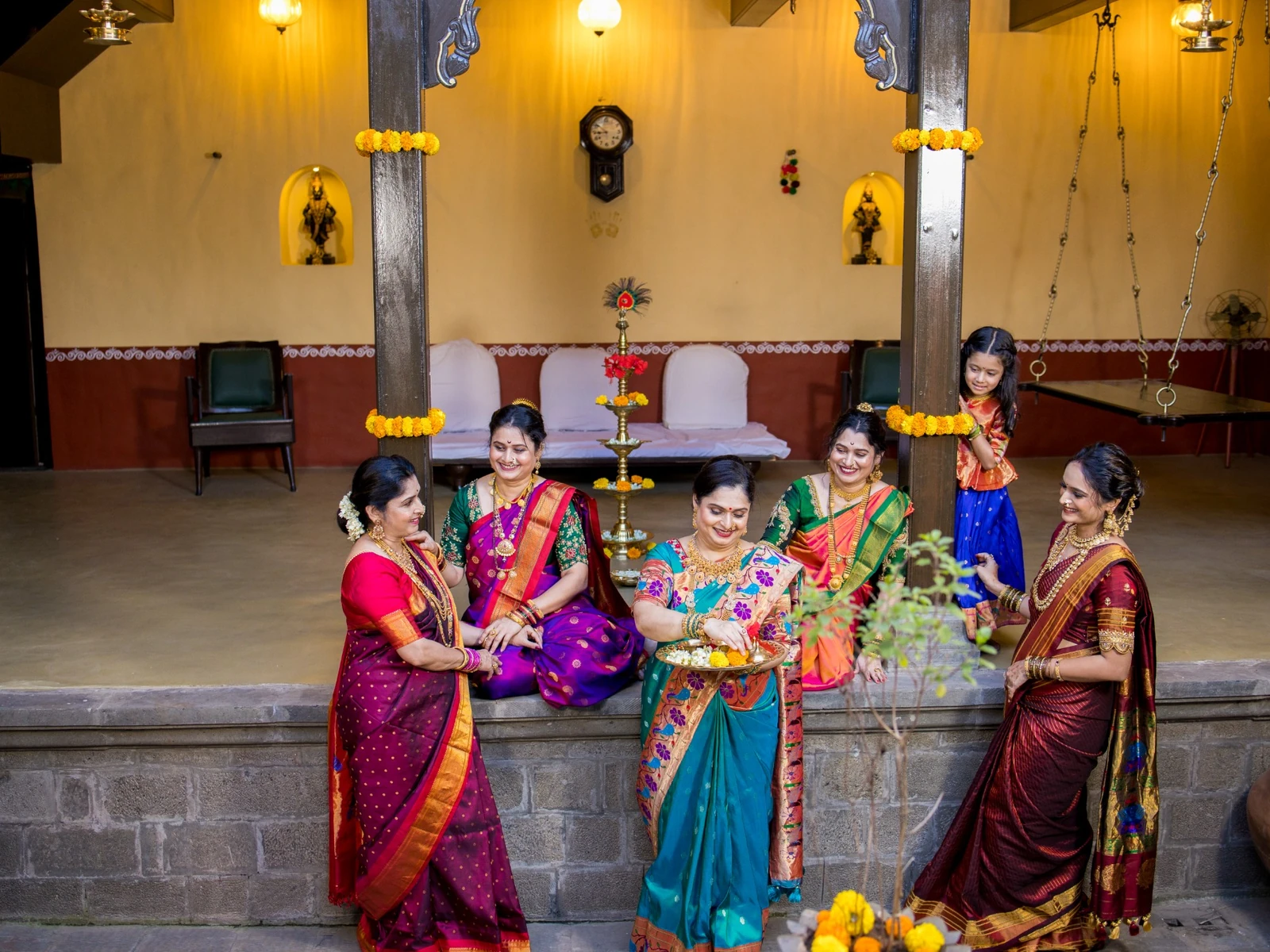 Festive celebration beside the courtyard tulsi vrindavan with teak pillars and wooden swing.