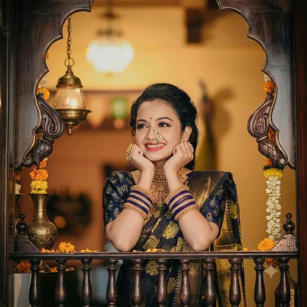 A bride in a navy-and-gold saree, nath and gold jewellery, framed in the wada's carved teak jharokha window with marigold garlands and a brass lantern beside her.